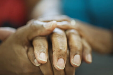 A black hospice patient and a black nurse hold hands in Torrance, CA.