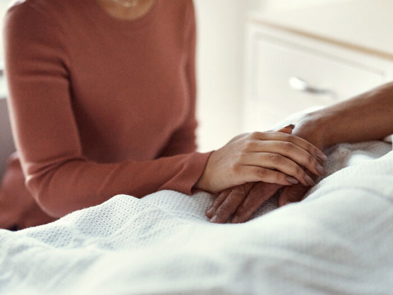 A family member holds a hospice patient's hand while in bed in LA or Orange County