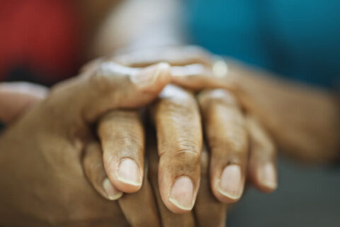 A black hospice patient and nurse hold hands in Torrance, CA.