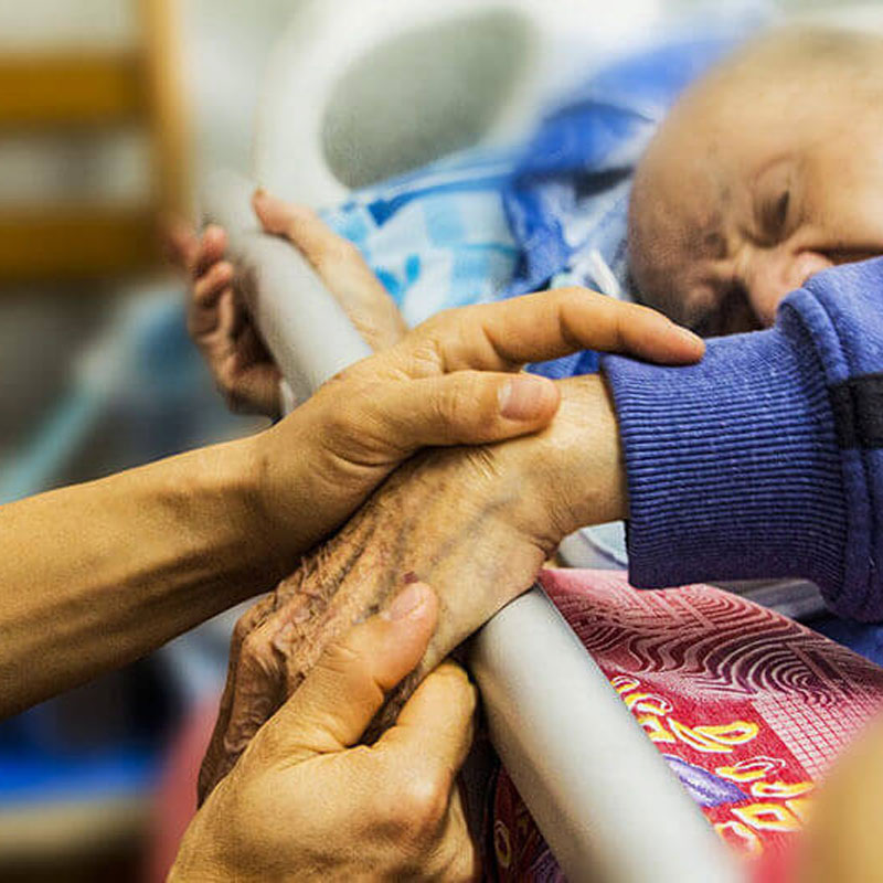 holding hands of elderly patient in bed