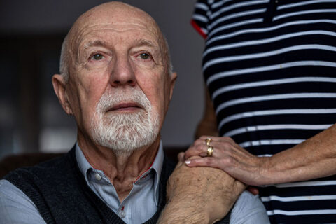 An elderly man with Alzheimer’s Disease holds his wife’s hand
