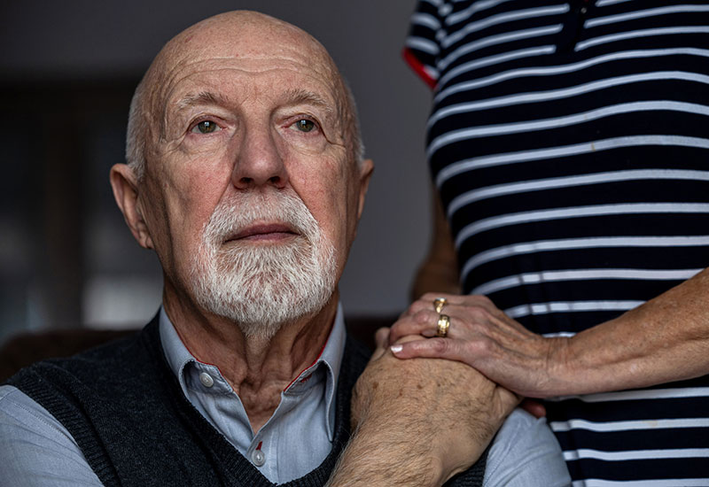 An elderly man with Alzheimer’s Disease holds his wife’s hand