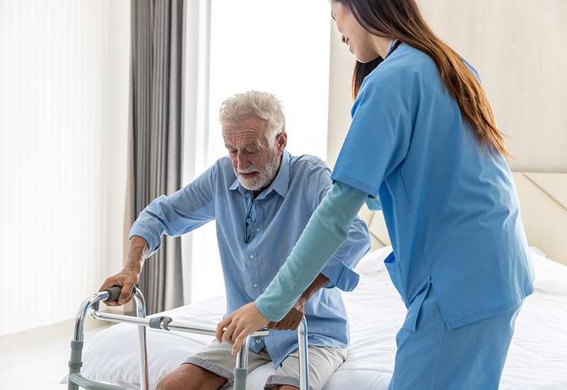 A home hospice nurse in Redondo Beach helps a senior man stand up with his walker