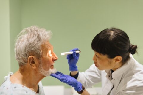 Care provider examining a patient’s eyes with a light during a hospice visit in Orange County