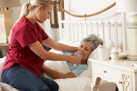 In‑home caregiver supporting an older adult near a window in Orange and LA Counties