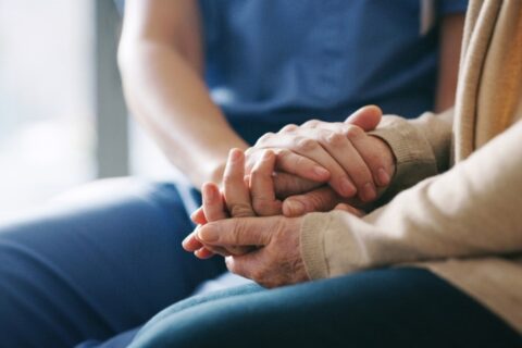 A caregiver holding hands with a patient while offering palliative care in Orange Counties