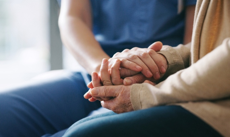 A caregiver holding hands with a patient while offering palliative care in Orange Counties