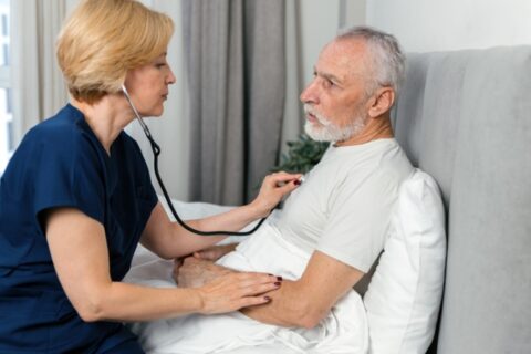 Clinician using stethoscope to check patient in bed in Orange Counties